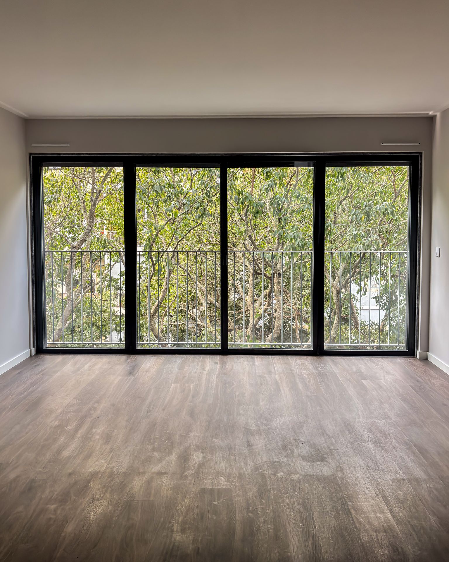 Sala com janela fixa ampla em alumínio preto e vista para arborização