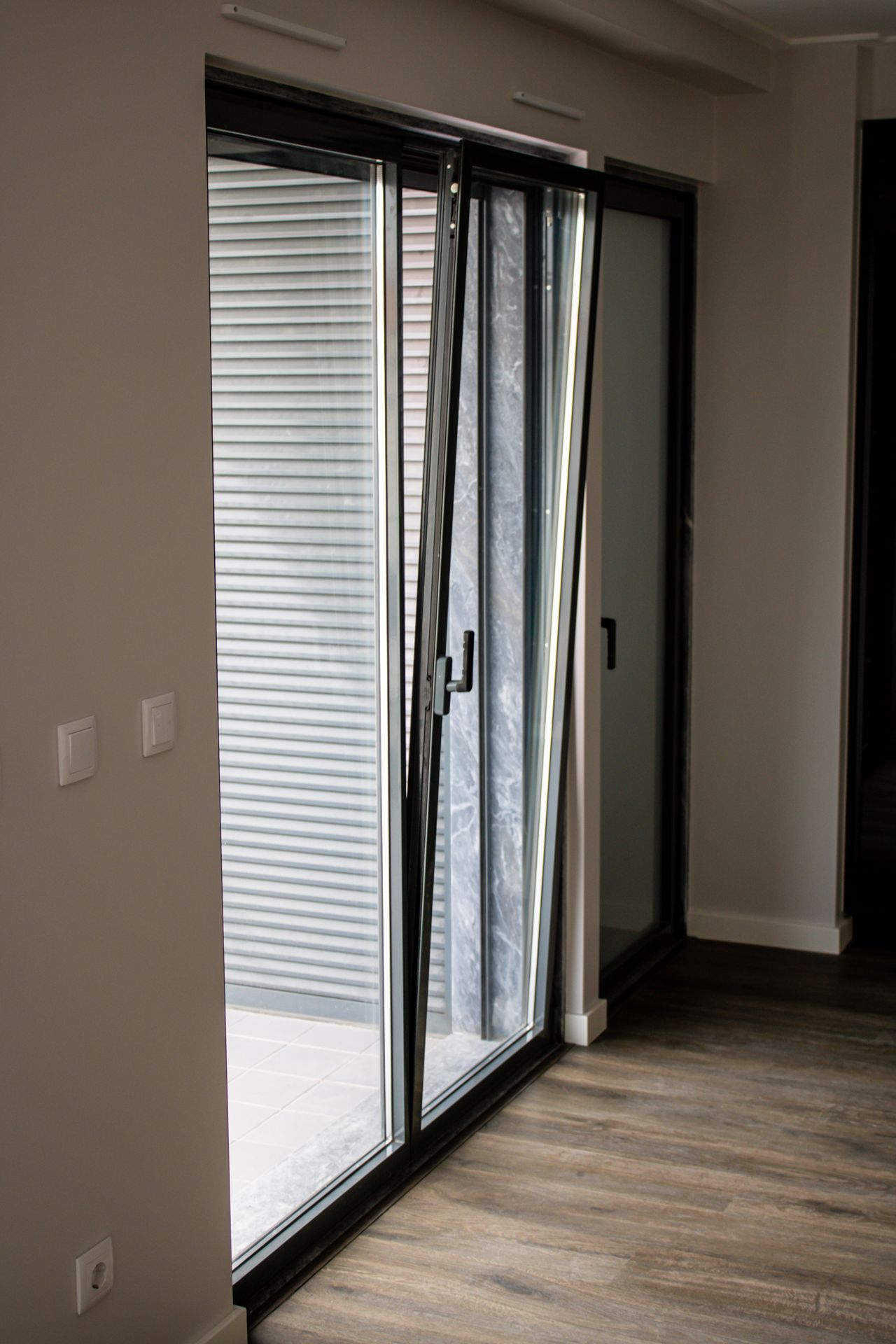 Porta de correr em alumínio preto com estore no interior de apartamento